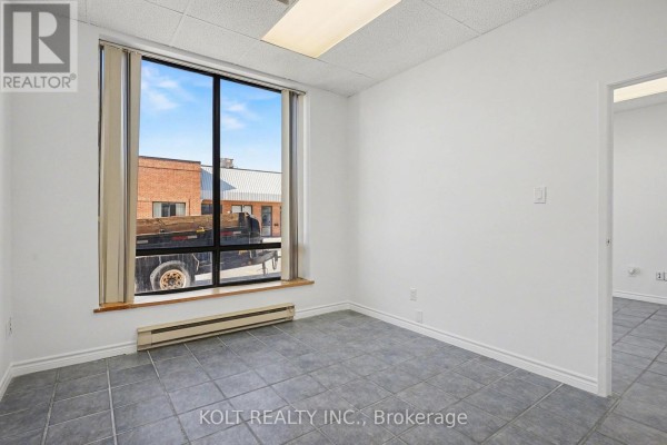 Empty commercial room with large window, grey tiled floor, and white walls. - 9 - 190 Britannia Road E, Mississauga