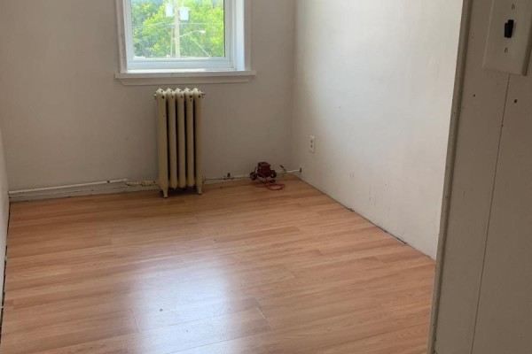Small room with light-colored walls, hardwood floor, and a radiator below a window with green trees outside. - 9 - 2 Bascom Street S, Uxbridge