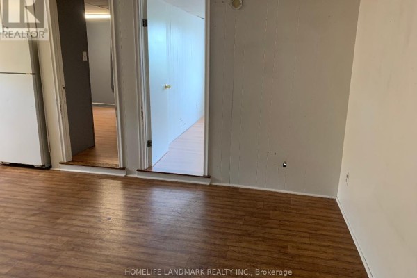 Interior view of a room with hardwood floors, connecting to another room and a kitchen area with a refrigerator. - 9 - 2 Bascom Street S, Uxbridge
