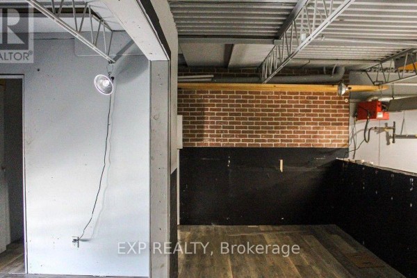 Interior of an unfinished space with light grey walls, brick accent wall, and wooden floor. - 9 - 30 Canvarco Road, Toronto