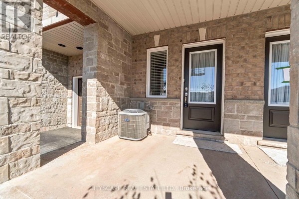 Covered concrete porch of a townhouse with an outdoor air conditioning unit and brown doors. - 9 - 40 Zinfandel Drive, Hamilton
