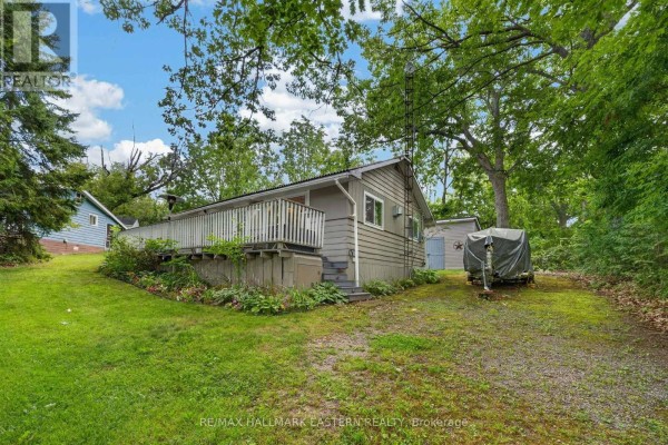 Side view of a grey cottage with a large wooden deck and surrounding greenery. - 9 - 422 Island View Road, Alnwick/haldimand