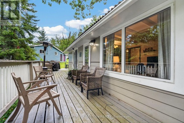 View of a wooden deck with chairs and a table, adjacent to a cottage with large windows. - 9 - 422 Island View Road, Alnwick/haldimand