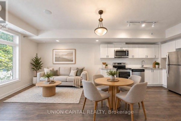 Open concept living and kitchen area with light grey sofa, round dining table, and white cabinets. - 9 - 6 Bicknell Avenue, Toronto