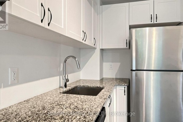 Kitchen counter with granite countertop, stainless steel refrigerator, and white cabinetry with black hardware. - 9 - 6 Bicknell Avenue, Toronto