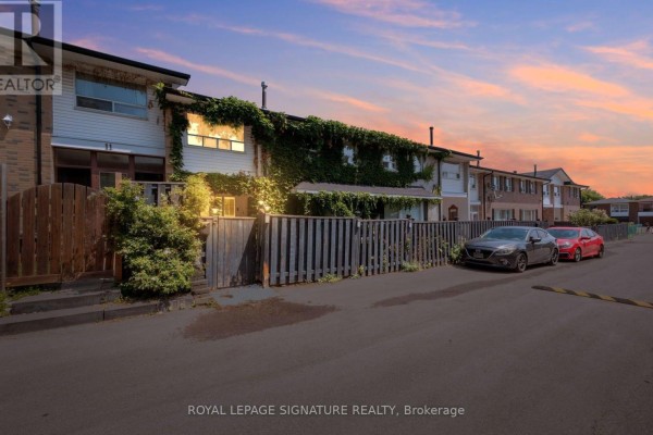 Row of townhouses with ivy facade, wooden fence and parked cars at dusk. - 9 - 61 Ardglen Drive, Brampton