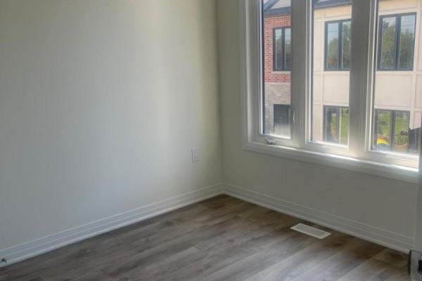 Empty room with white walls, wood-look laminate flooring, and a large window overlooking the street. - 9 - 726 Front Royal Street, Mississauga