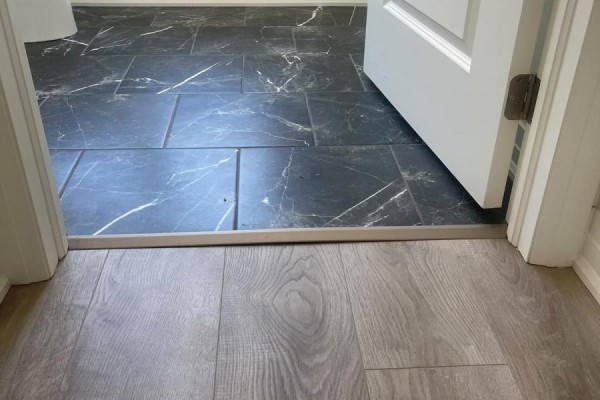 Transition between light wood-look laminate flooring and dark marble-patterned tile flooring in a doorway. - 9 - 726 Front Royal Street, Mississauga