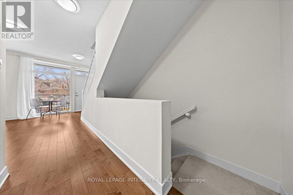 Interior hallway with wooden floors, white walls, and a staircase leading upstairs, with a small table by a window. - 9 - 78 Holmwood Avenue, Ottawa