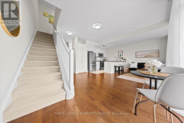 Living area and kitchen with wooden floors, carpeted stairs, stainless steel appliances, and a dining table. - 9 - 78 Holmwood Avenue, Ottawa