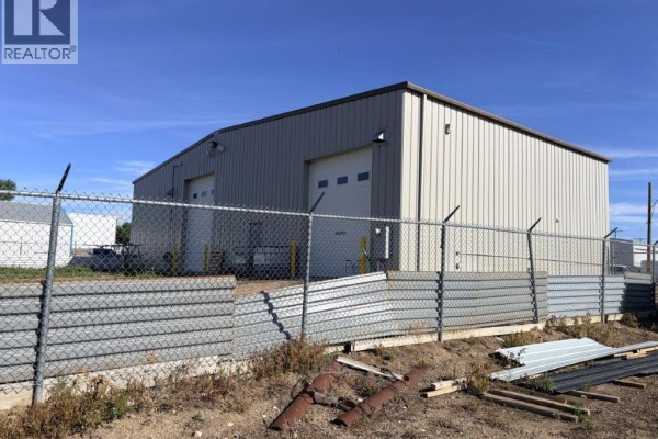 Side view of the metal commercial building with a chain-link fence and metal barrier in the foreground. - 9 113 4th Street, Kindersley