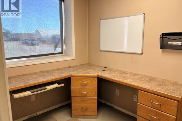 Corner office desk with a keyboard tray, drawers, and a window overlooking the exterior. - 9 113 4th Street, Kindersley