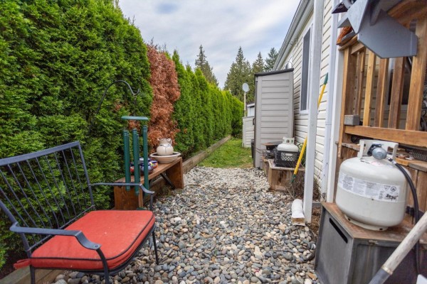 Side yard of the mobile home with a red cushioned chair, pebble ground, and a propane tank. - 9 14600 Morris Valley Road, Mission