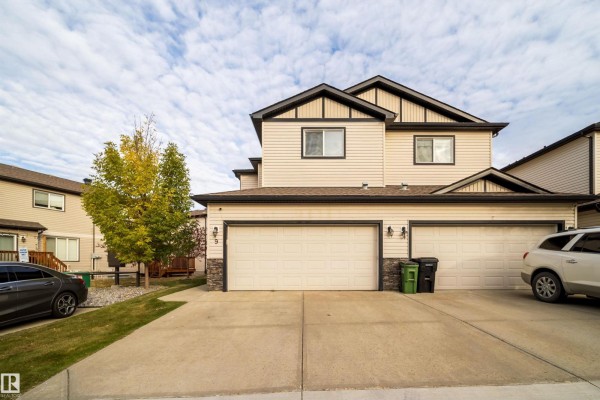 Front view of a duplex building with beige siding, dark trim, and two attached garages. - #9 445 Brintnell Bv Nw Nw, Edmonton