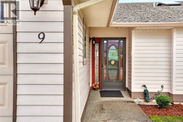 Close-up of the townhouse entrance with a stained-glass door and beige siding. - 9 5608 Strathcona St, Port Alberni