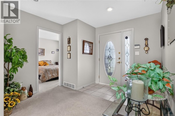 Foyer with light grey walls, beige carpet, and a doorway leading to a bedroom. - 9 5608 Strathcona St, Port Alberni