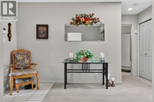 Foyer with a patterned armchair, glass console table, and a mirror on the wall. - 9 5608 Strathcona St, Port Alberni
