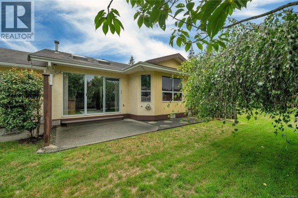 Rear view of townhouses with large sliding glass doors, a concrete patio, and backyard grass. - 9 605 Rockland Rd, Campbell River