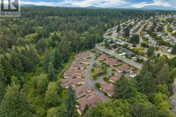 Aerial view of a townhouse complex nestled beside a dense forest and suburban neighborhood. - 9 605 Rockland Rd, Campbell River