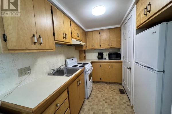 Kitchen with light wood cabinets, white appliances, and checkered floor. - 9 Aberdeen St S, Chapleau