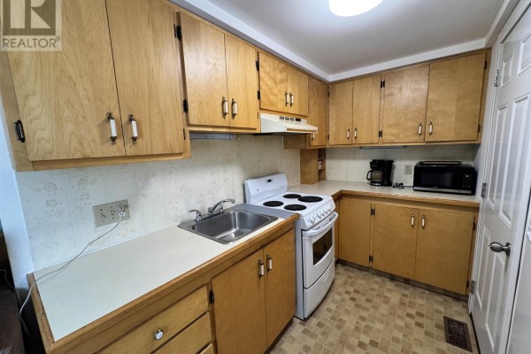 Kitchen with light wood cabinets, stainless steel sink, and white stove. - 9 Aberdeen St S, Chapleau