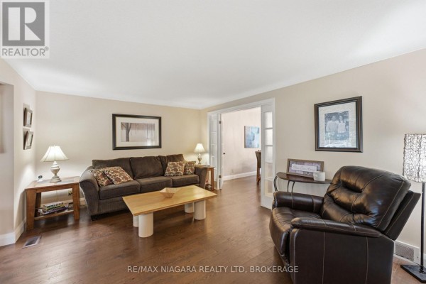 Living room with beige walls, dark hardwood floors, a brown sofa, and a leather recliner. - 9 Beechnut Court, Pelham