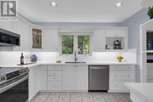 White kitchen with subway tile backsplash, stainless steel appliances, and a window overlooking greenery. - 9 Cabell Road, Tiny