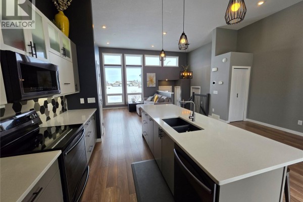 Open-concept kitchen with an island, stainless steel appliances, and a living area view. - 9 Carl Drive, Meadow Lake
