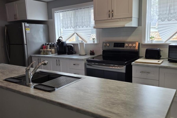 Kitchen island with sink and faucet, white cabinets, and stainless steel stove with oven. - 9 Central Ave, Elliot Lake