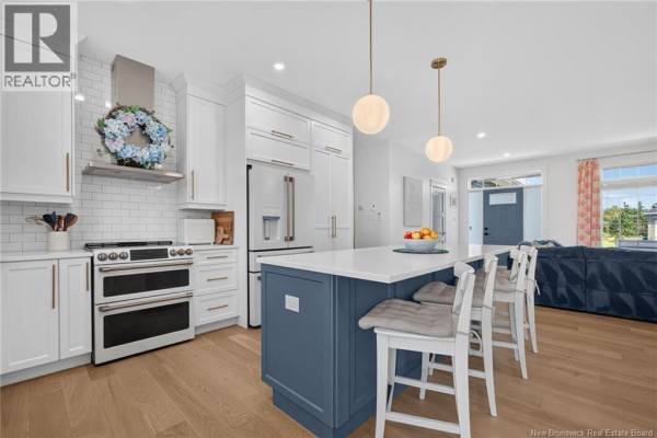 Modern kitchen with white cabinetry, a blue island with bar stools, and hardwood floors. - 9 Congressional Crescent, Moncton