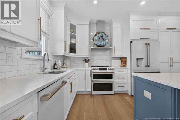 Kitchen view showcasing white subway tile backsplash, stainless steel appliances, and a large refrigerator. - 9 Congressional Crescent, Moncton