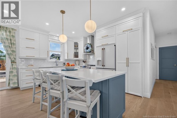Open-concept kitchen and living area with a blue island, pendant lights, and large windows. - 9 Congressional Crescent, Moncton