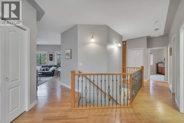 Hallway with light wood floors, grey walls, and a wooden staircase with a metal railing. - 9 Creek Road, Rural Ponoka County