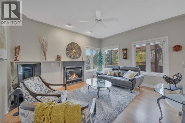 Living room with a fireplace, grey sofa, patterned armchair, and glass coffee table. - 9 Creek Road, Rural Ponoka County