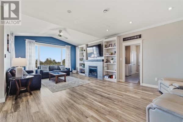Living room with a vaulted ceiling, large window, fireplace, built-in shelves, and hardwood floors. - 9 Crestview Place, St  John S