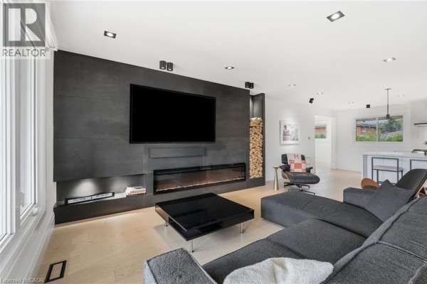 Living room with large TV, modern fireplace, grey sectional, and wood accents. - 9 Donlea Drive, Hamilton