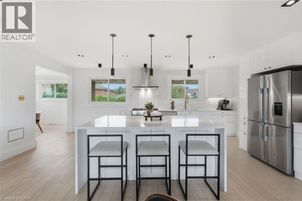 Bright kitchen island with three stools, stainless steel refrigerator, and windows view. - 9 Donlea Drive, Hamilton