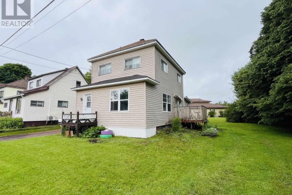 Side view of a two-story house with beige siding, wooden deck, and trees. - 9 Dundonald Street, Amherst