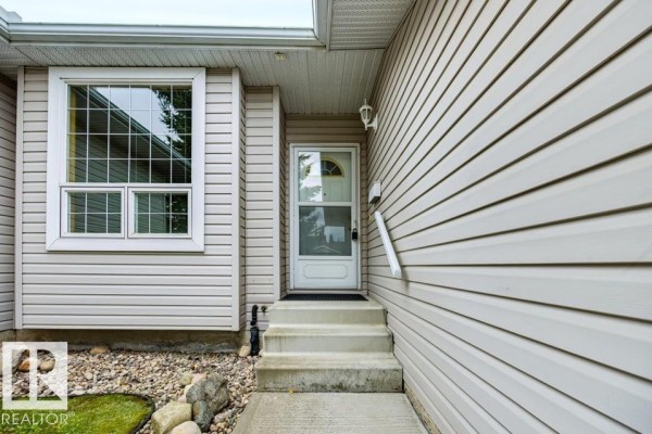 Front entrance of the duplex with beige siding, white door, and a large window. - 9 Hillcrest Co, Spruce Grove