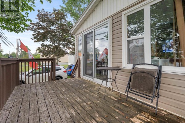Exterior view of a house from the street, with a driveway, deck, and trees. - 9 Main Street East, Stewiacke