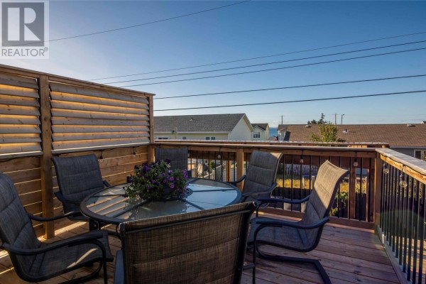 Circular glass dining table with chairs on a wooden deck with a slatted wood privacy screen and railing. - 9 Mercedes Court, Conception Bay South
