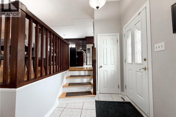 Entrance hall with a white door, tiled floor, and wooden stairs leading up. - 9 Stanley Street, Campbellton