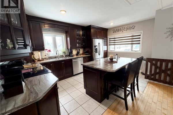 View of the kitchen island with bar stools, dark wood cabinets, and tiled flooring. - 9 Stanley Street, Campbellton