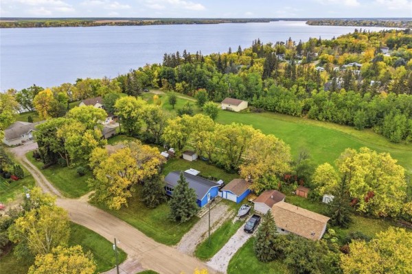 Aerial view showing the blue house, garage, and the nearby lake in the background. - 9 Tanco Crescent, Lac Du Bonnet