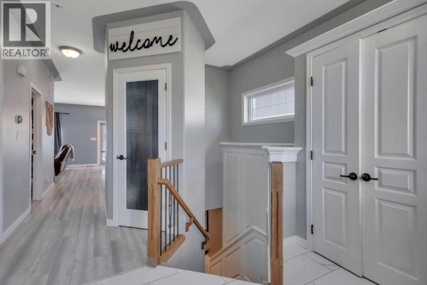 Interior hallway with light grey walls, wood staircase, and white double doors. - 9 Valley Crescent, Blackfalds