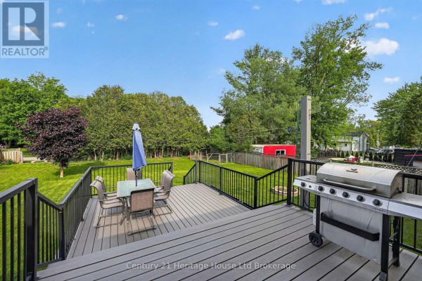 Deck with outdoor dining furniture and a grill, overlooking a grassy backyard with mature trees and a clear blue sky. - 9 West Street N, Norwich