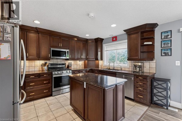 Dark wood kitchen with stainless steel appliances, granite island, tiled backsplash, and beige tile flooring. - 9 West Street N, Springford