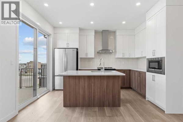 Open-concept kitchen featuring white upper cabinets, wood lower cabinets, a central island, and a sliding glass door. - 9 Wild Rose Bay Sw, Airdrie