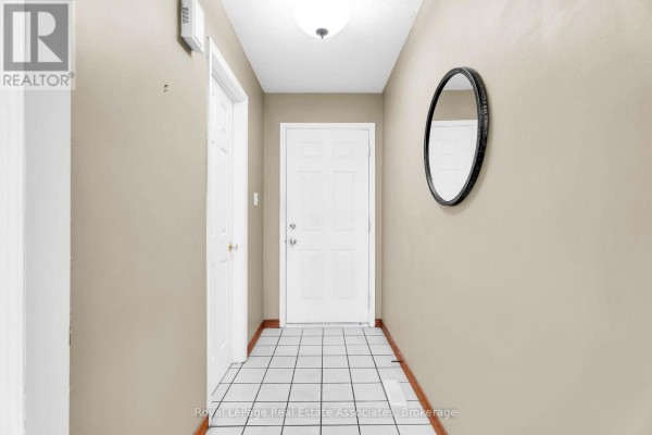 Interior hallway with beige walls, white tiled floor, a white door, and an oval mirror on the wall. - 9 Windwood Drive, Toronto