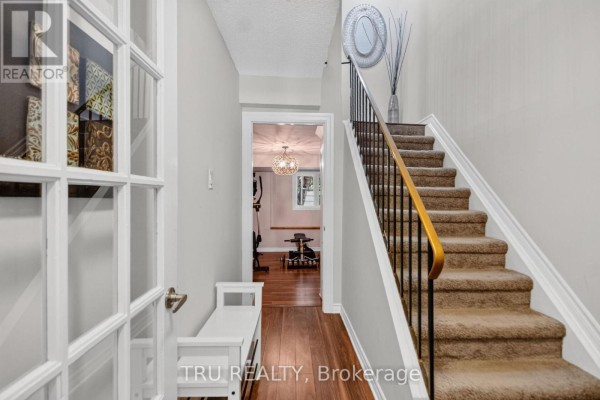 Hallway with stairs leading up and a doorway to a finished basement. - 90 - 50 Lightfoot Place, Ottawa